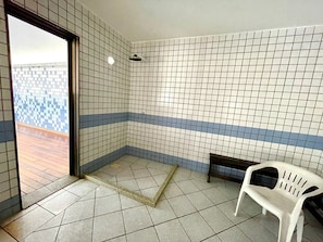 Una habitación con paredes de baldosas, un banco y una puerta que da al exterior.