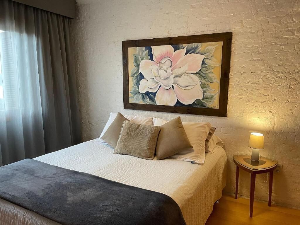 Una habitación de hotel con una cama, almohadas, una lámpara y un cuadro en la pared.