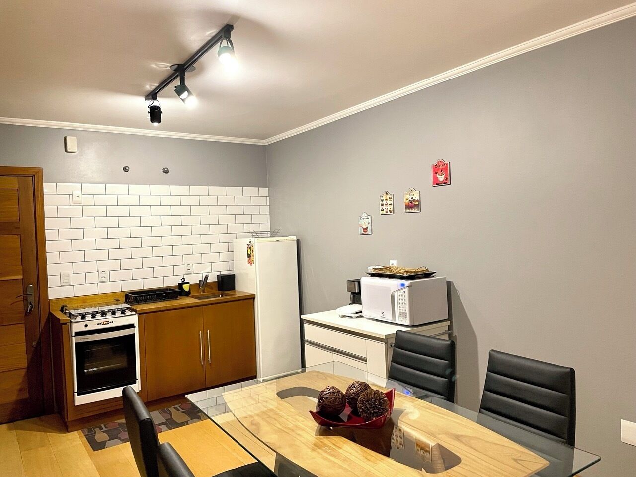 A compact kitchen with a stove, oven, microwave, and refrigerator. There is a dining table with chairs and a small decorative bowl on the table.