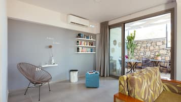 Una sala de estar moderna con una pared gris, una estantería, un sillón de mimbre, un otoman azul y un sofá estampado.