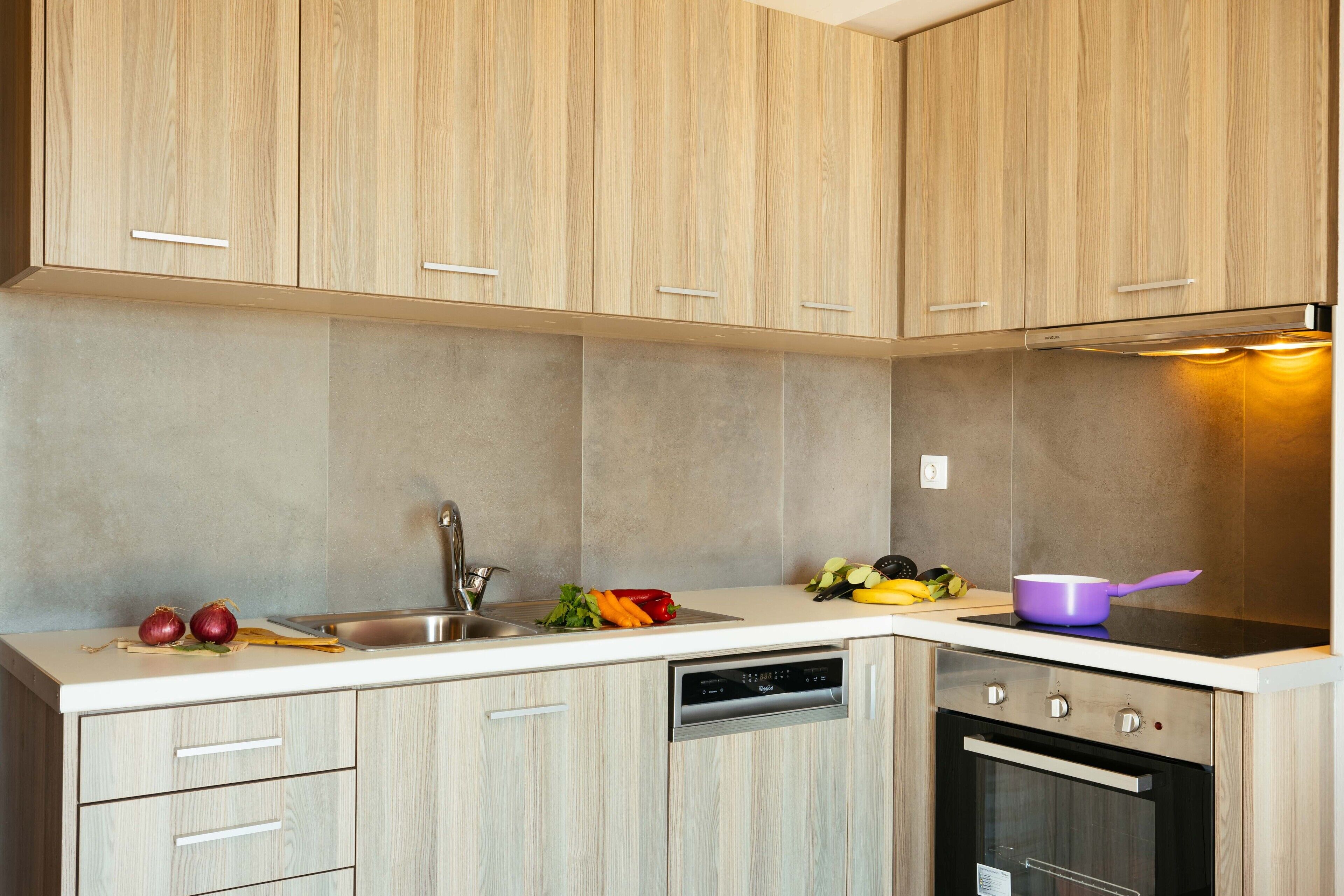 A modern kitchen with light wood cabinets, a stainless steel sink, and a built-in dishwasher.