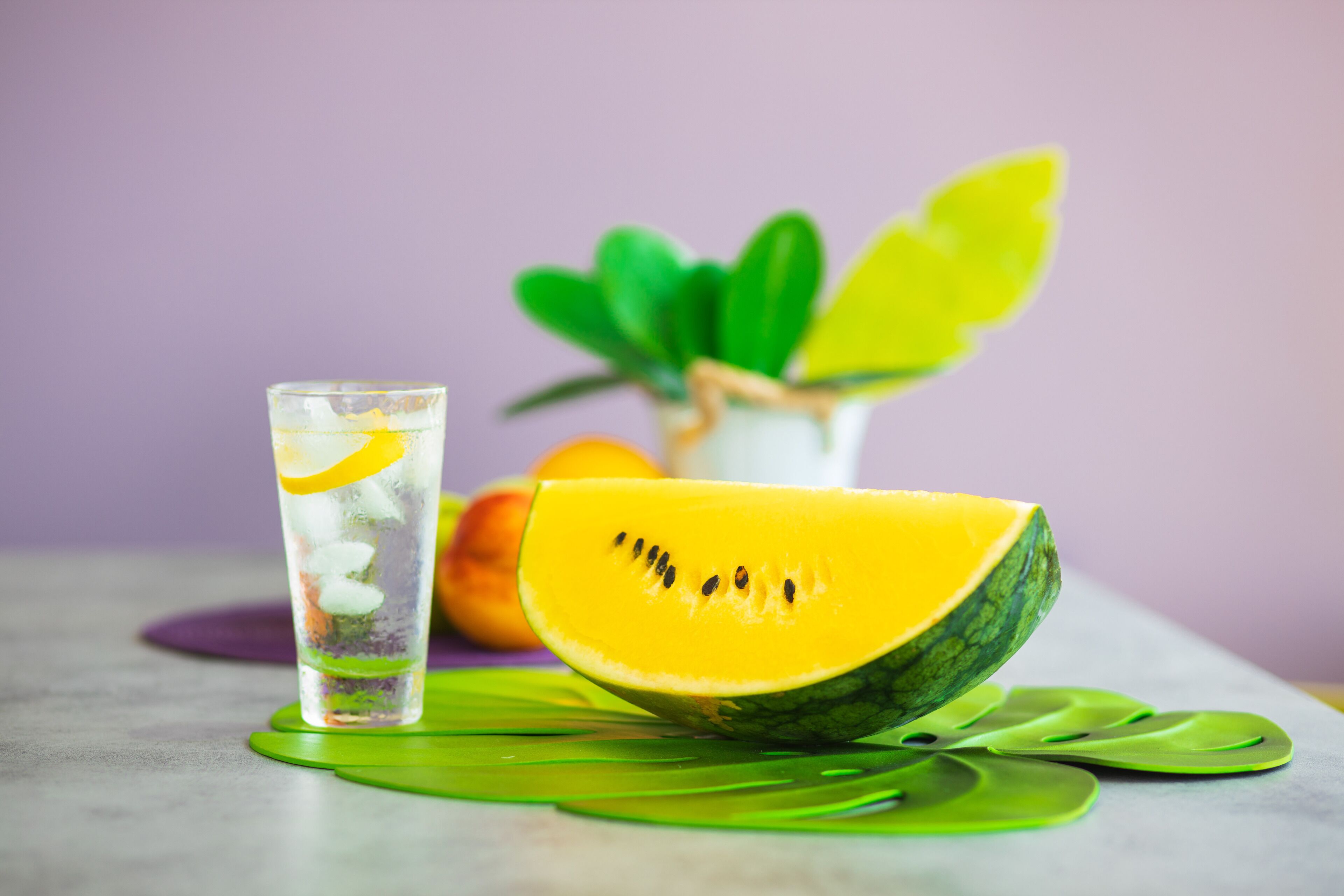 Un verre d’eau avec une tranche de fruit, un fruit entier et une plante.
