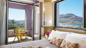 Habitación de hotel con cama, una mesita con sillas, ventana con vista a la montaña y balcón con una silla.