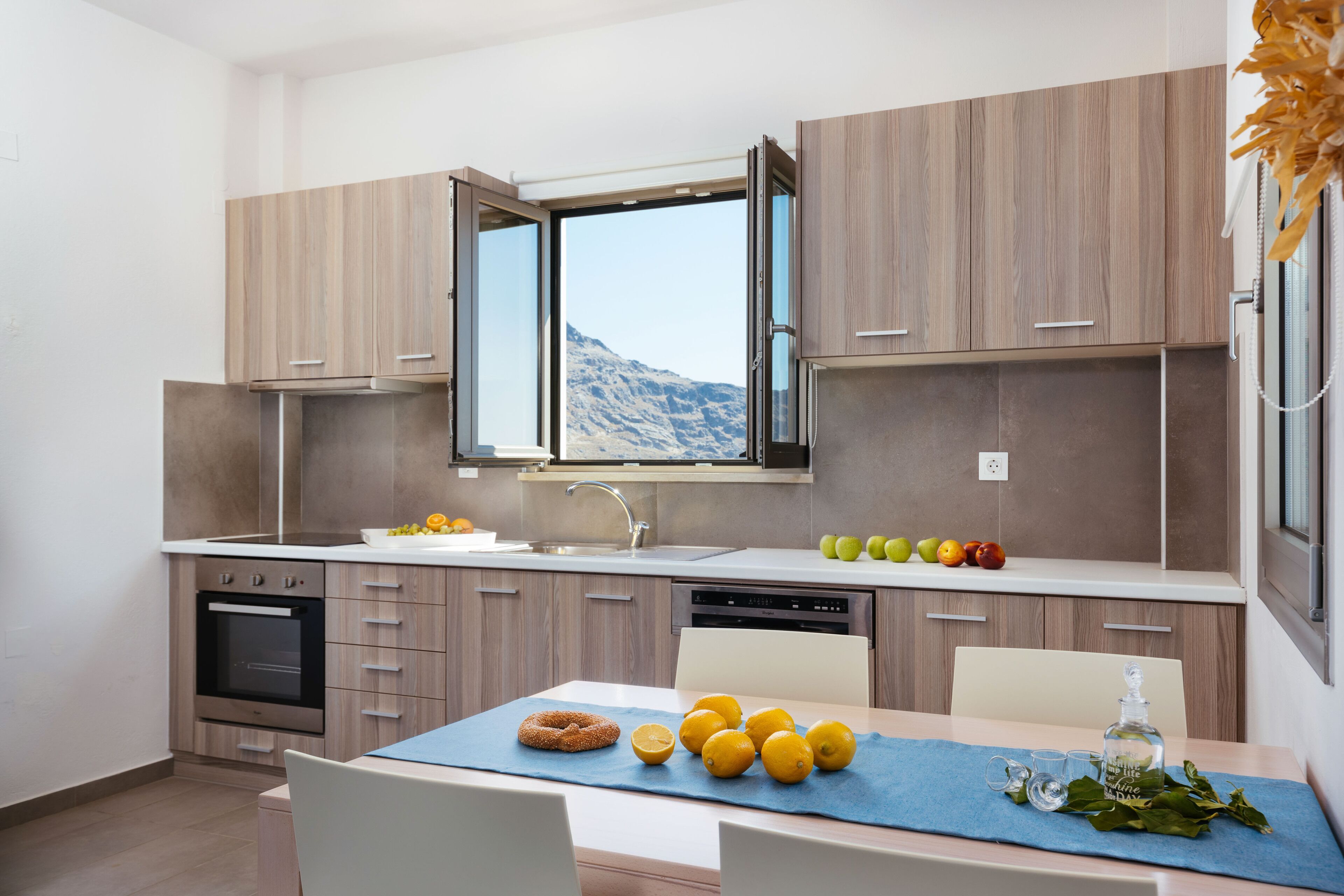 A modern kitchen with wooden cabinets, a built-in oven, and a large window overlooking a mountainous landscape.