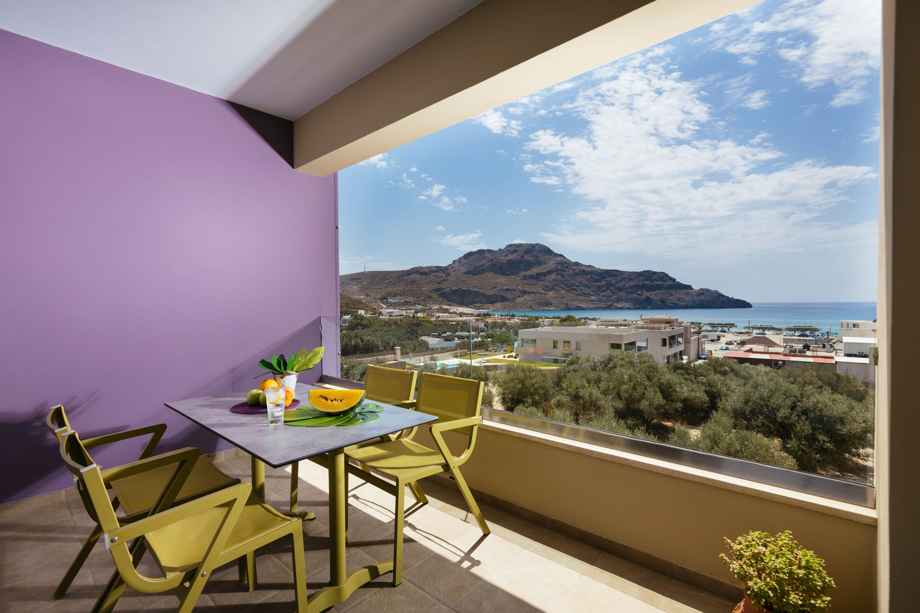Un balcon avec une table et des chaises, un pot de fleurs et une vue sur une montagne et la mer.