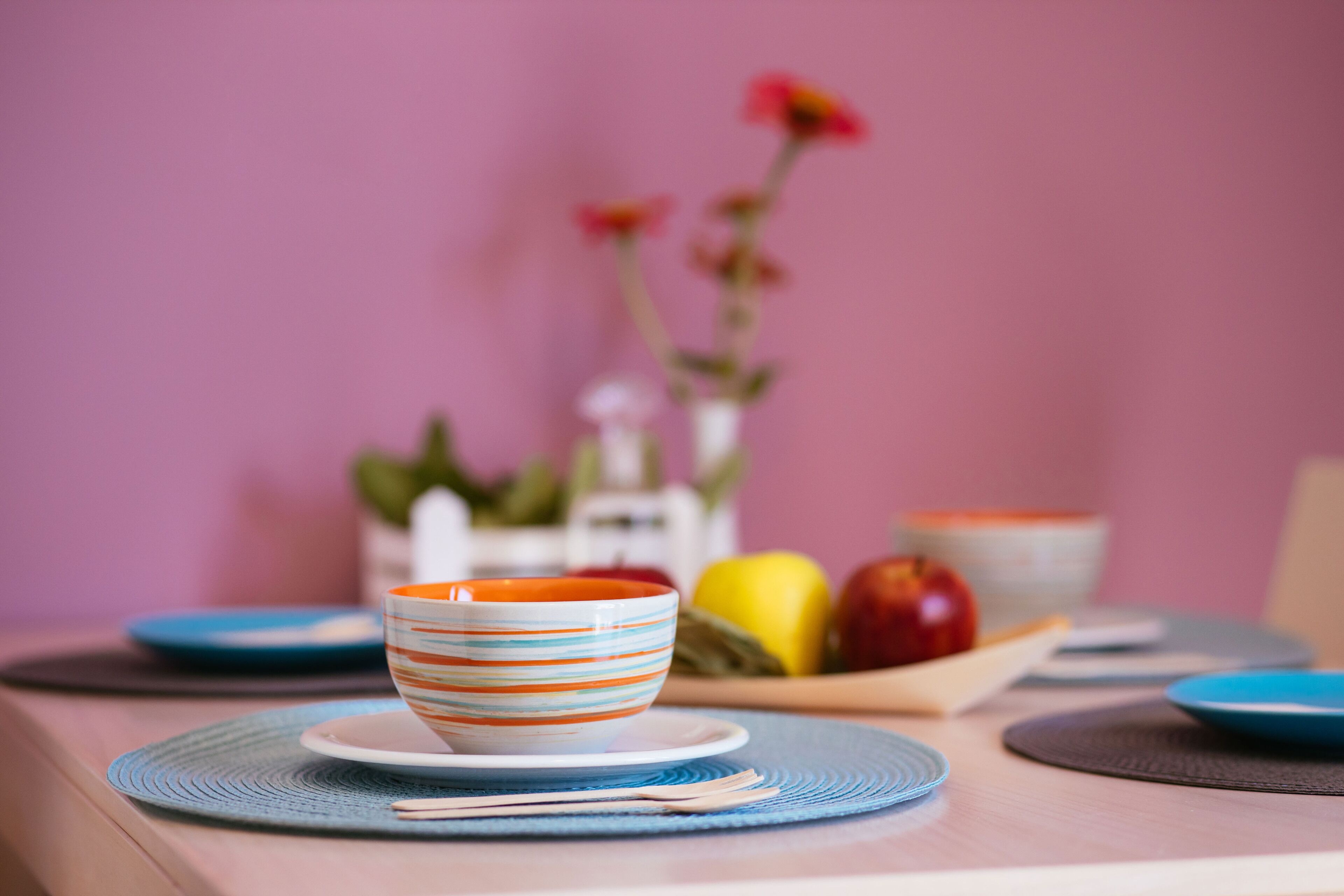 Una mesa con un bol estampado, platos y una cesta de frutas.