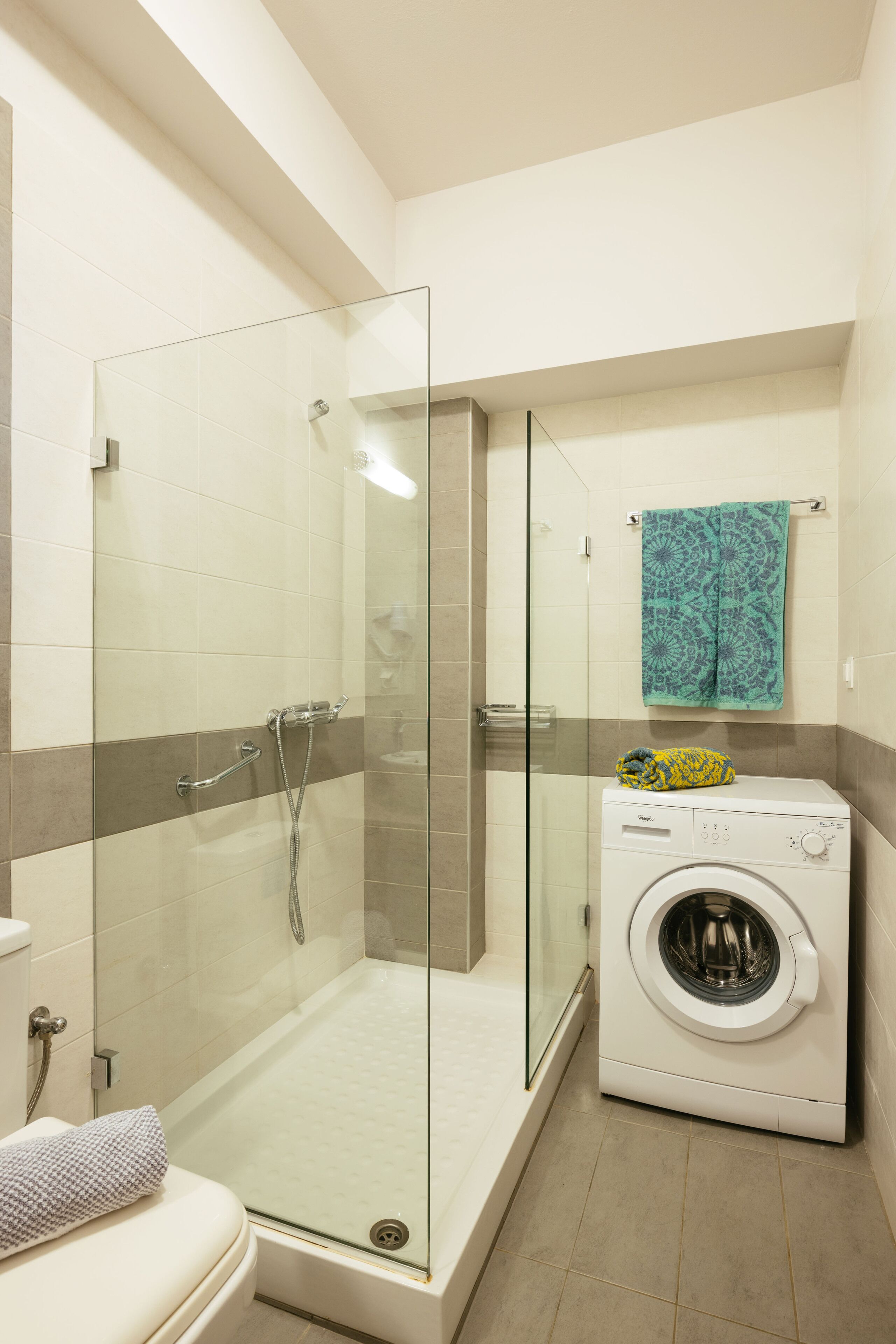 A bathroom with a glass-enclosed shower, a washing machine, and a toilet.