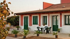 A two-story building with a tiled roof, green shutters, and a small patio with a table and chairs. - Agriturismo Arangea (Lequile)