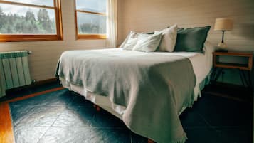 Un dormitorio con una cama, una ventana, un radiador y una mesita de noche con una lámpara.
