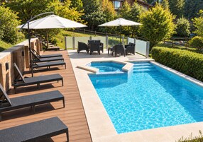 Una piscina con sillas de descanso y sombrillas, rodeada de follaje.