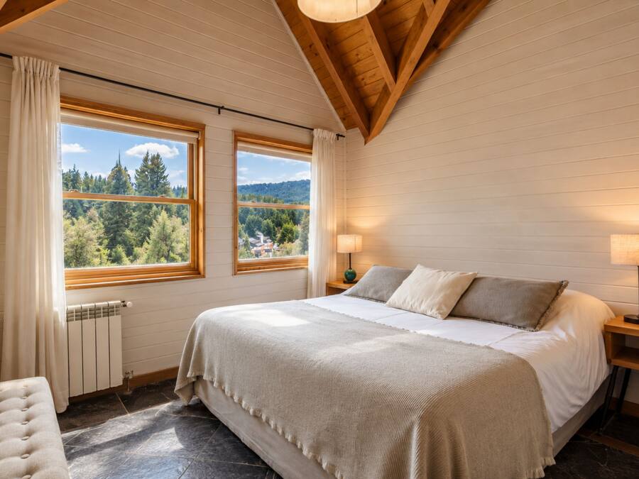 Een slaapkamer met een groot bed, twee ramen, een radiator en een nachtkastje met een lamp.