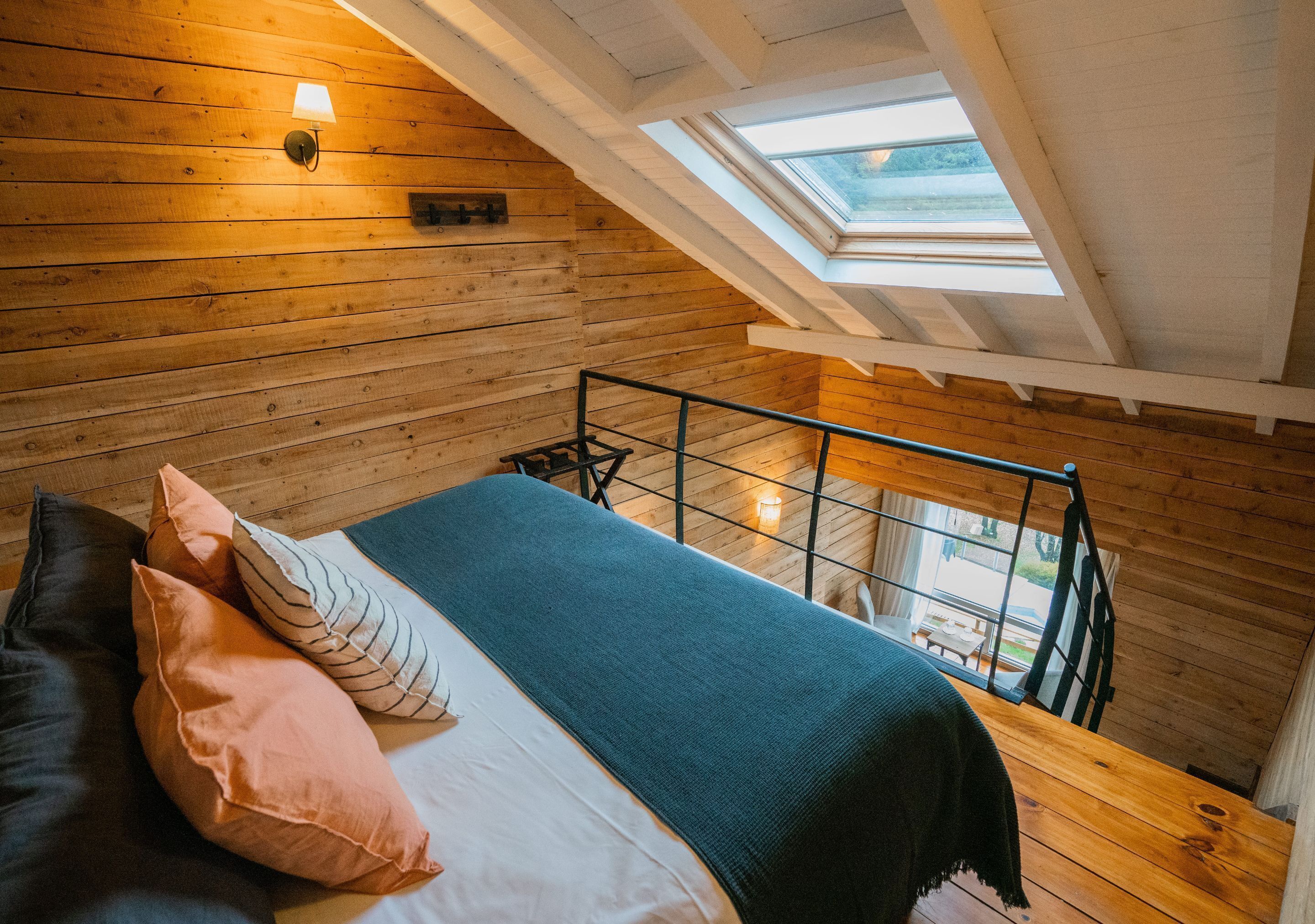 A loft bedroom with a sloped ceiling, a skylight, a bed with pillows, and a view of the outdoors.