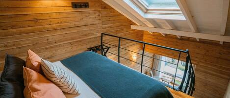 A loft bedroom with a sloped ceiling, a skylight, a bed with pillows, and a view of the outdoors.