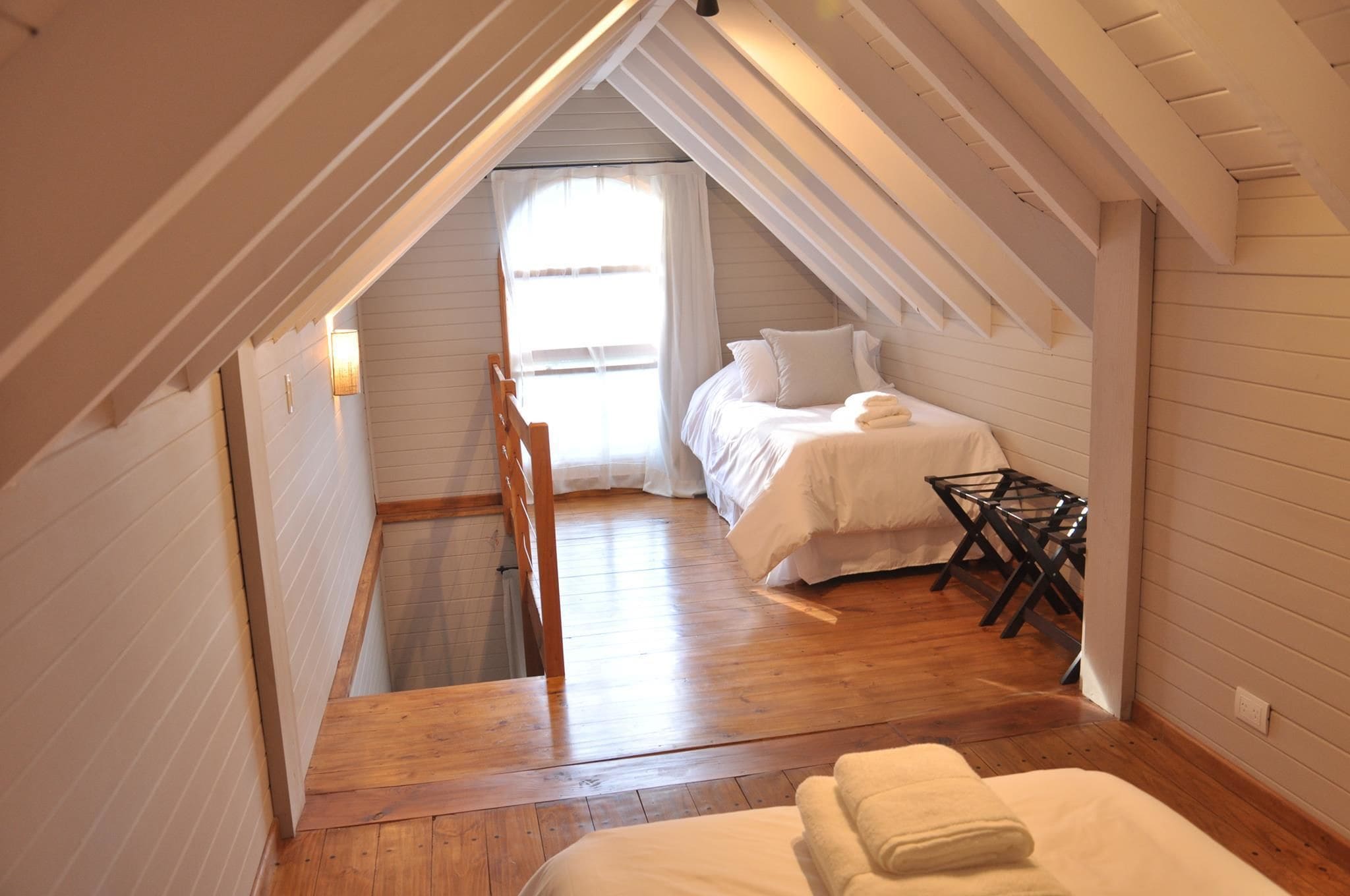 A cozy attic bedroom with a sloped ceiling, wooden flooring, and a bed with white bedding.