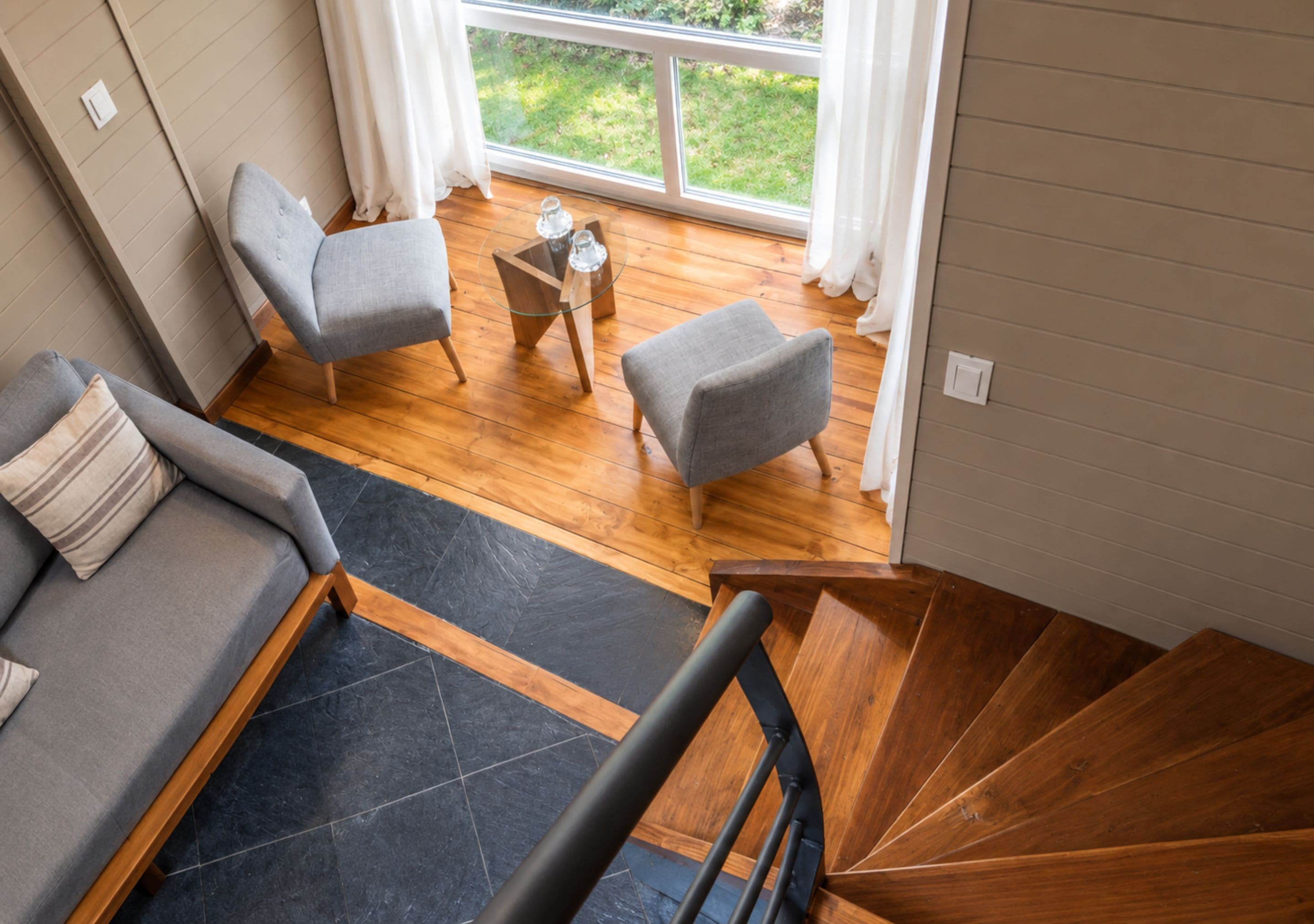Un intérieur moderne avec un escalier en bois, des canapés gris et une petite table sur laquelle sont disposés des verres.