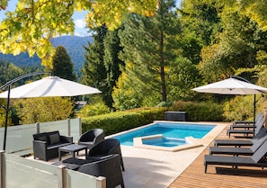 A poolside area with lounge chairs and umbrellas, surrounded by lush greenery and a mountainous backdrop. - Hosteria Verde Morada (Villa La Angostura)