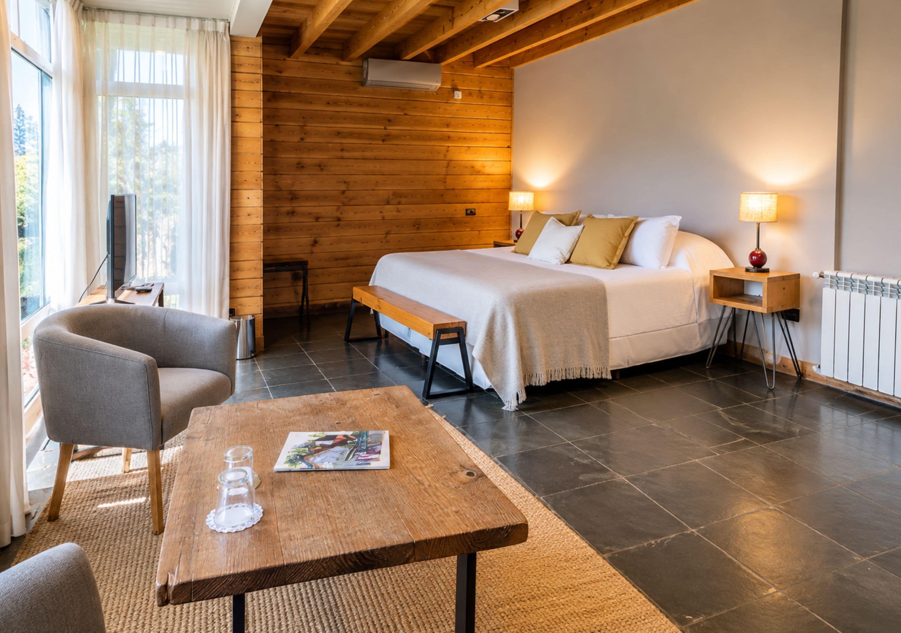 Una habitación de hotel con cama, mesitas de noche, escritorio, silla y ventana con cortinas.