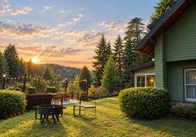 Un patio con mobiliario exterior, una parrilla y vistas a un área boscosa con una casa al fondo.