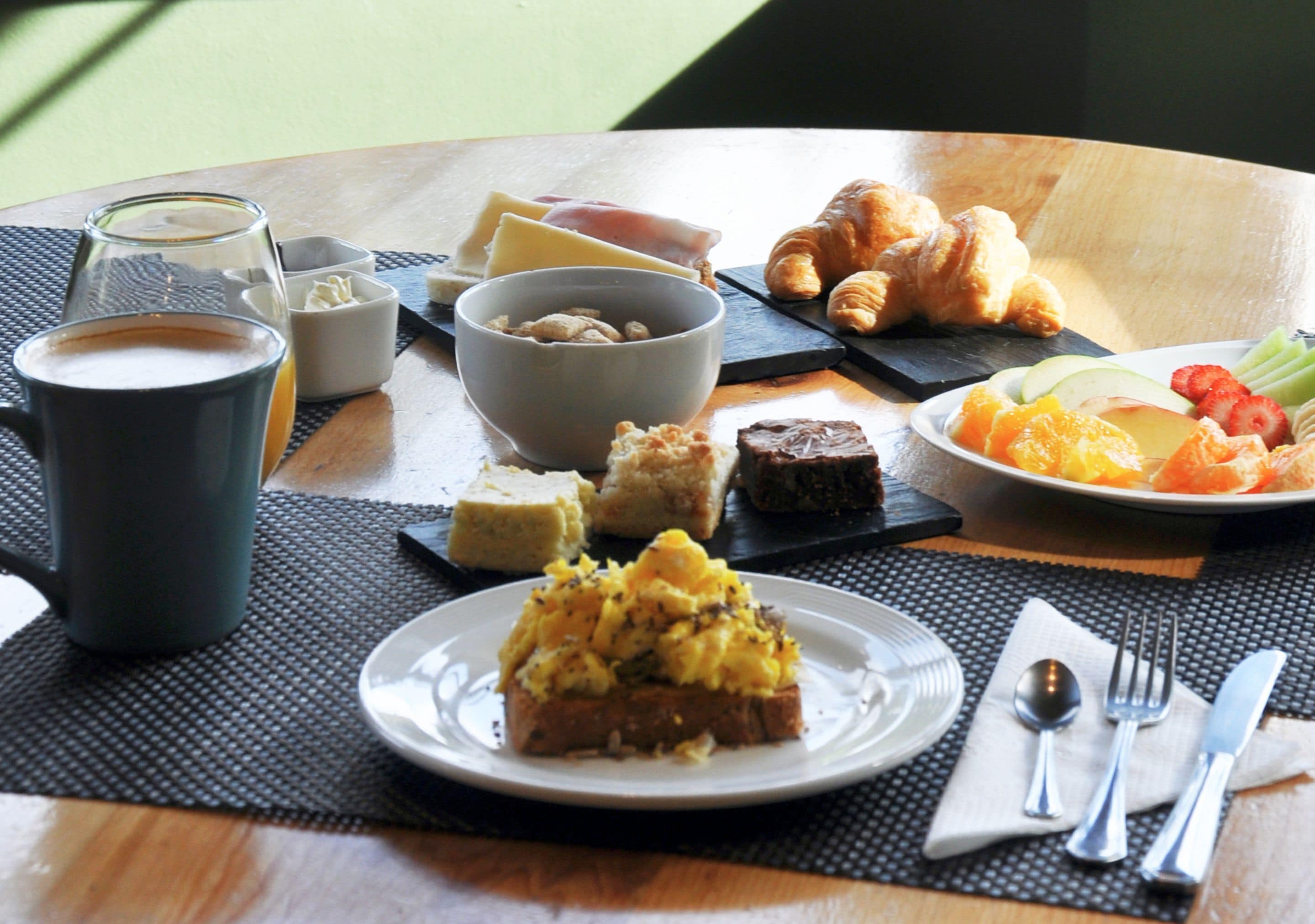 A breakfast setting with a croissant, fruit, and a coffee cup on a table.