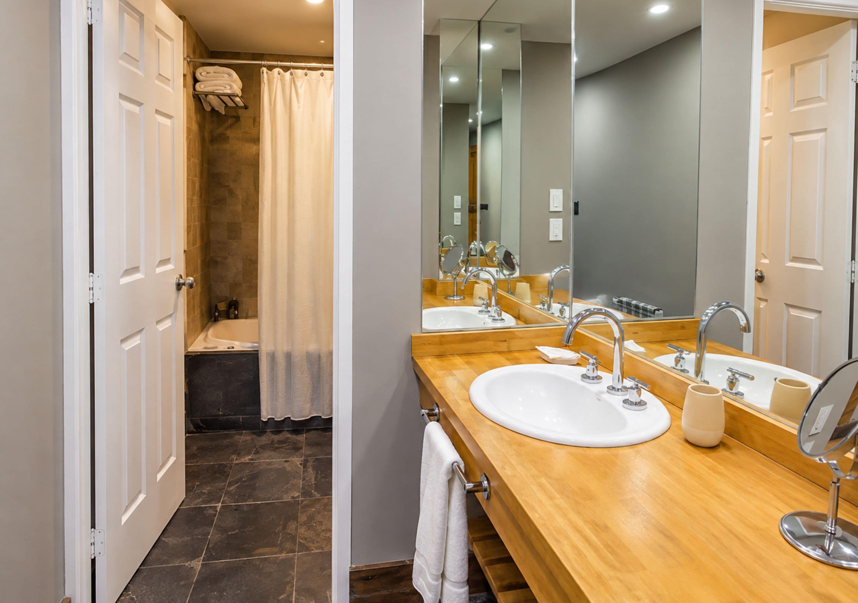 A modern bathroom with a wooden vanity, two sinks, a bathtub, and a shower with a beige curtain.