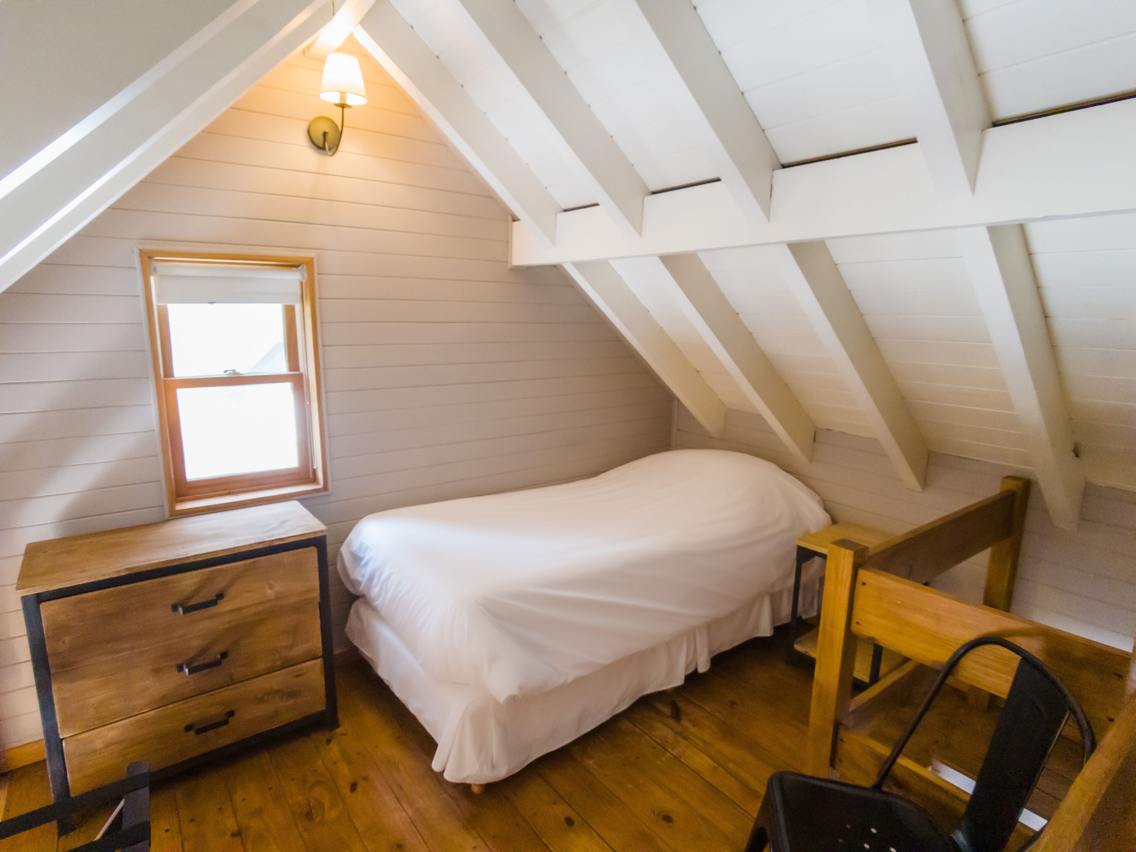 Un dormitorio acogedor en un ático, con una cama individual, una mesita de noche, un aparador y una ventana.
