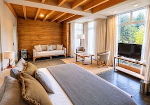 A hotel room with a large bed, a sofa, a chair, a TV, and a window with a view of trees. - Hosteria Verde Morada (Villa La Angostura)