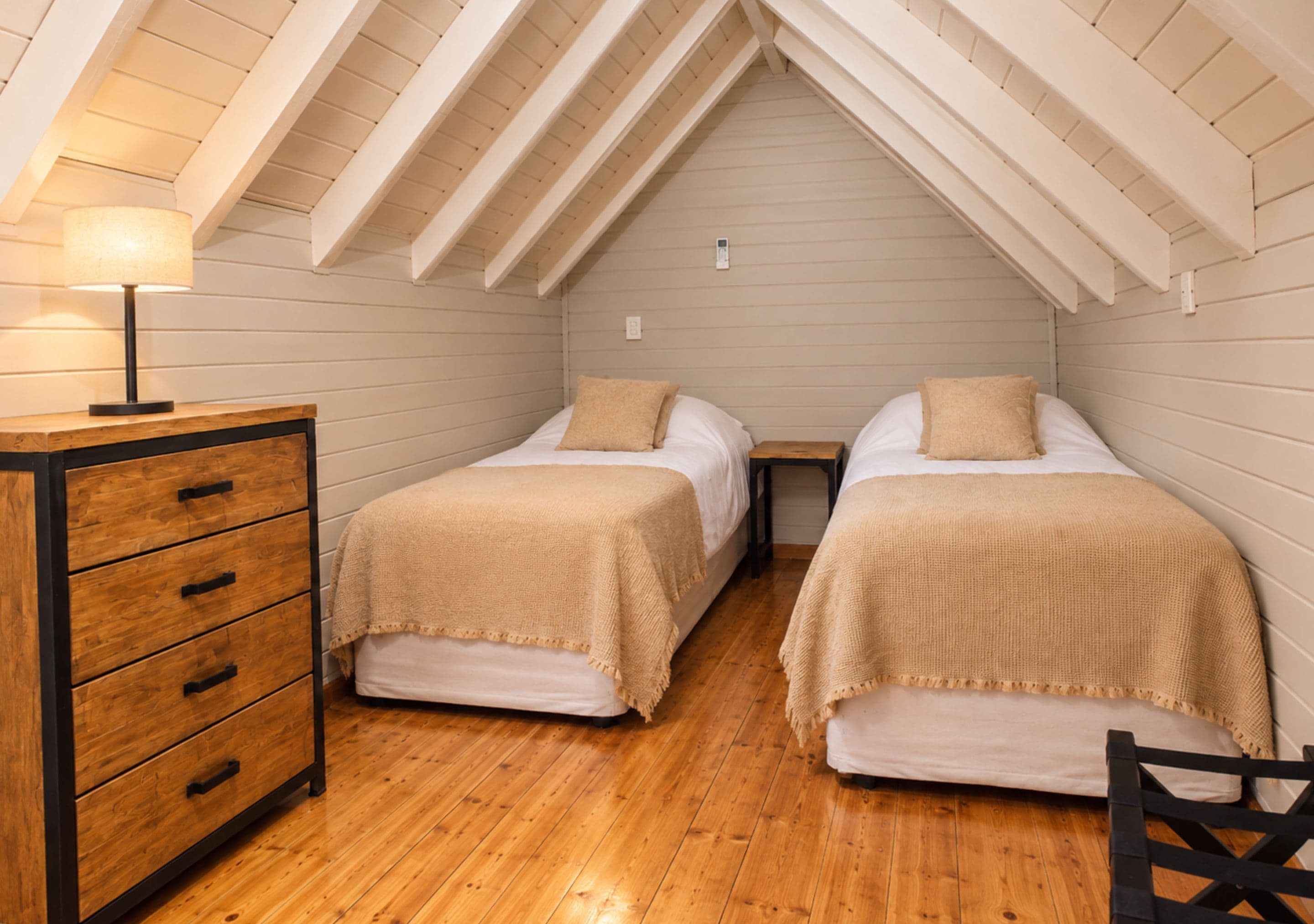 A small, cozy room with two beds, a wooden dresser, and a lamp.