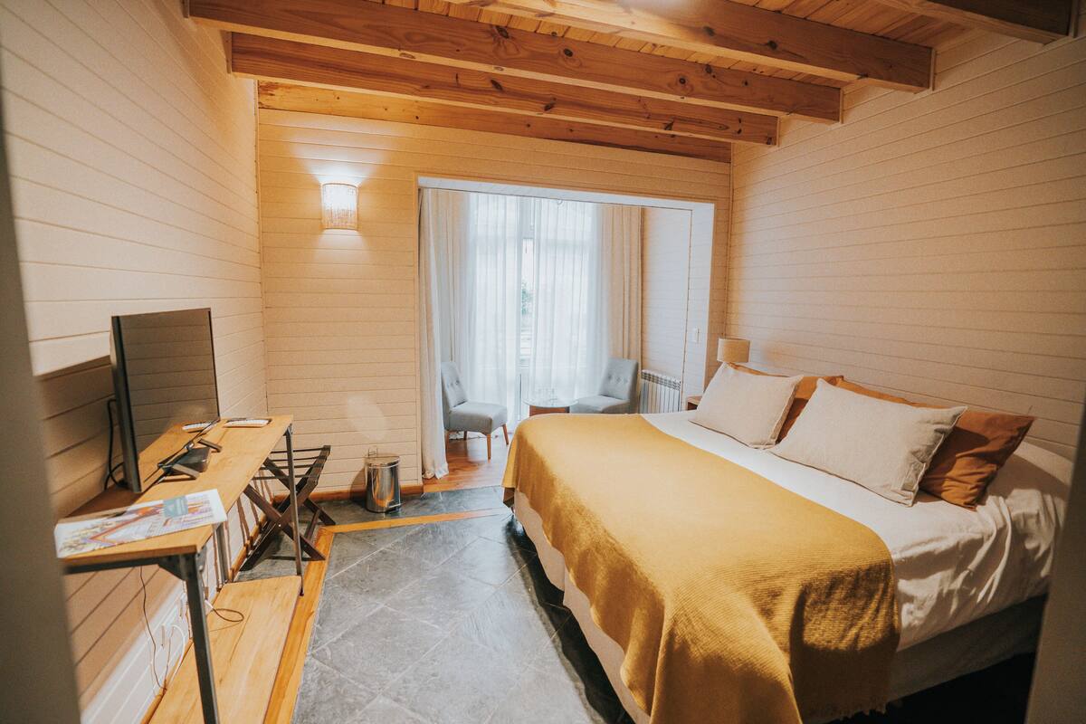 A hotel room with a bed, a desk, a chair, a TV, and a window with curtains.