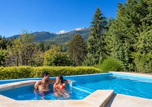 A swimming pool with a mountain view, surrounded by trees and a hedge. - Hosteria Verde Morada (Villa La Angostura)