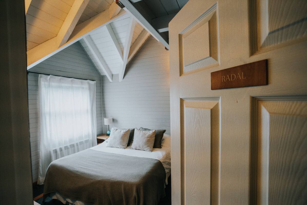 A bedroom with a bed, a nightstand, a lamp, and a door with a sign.