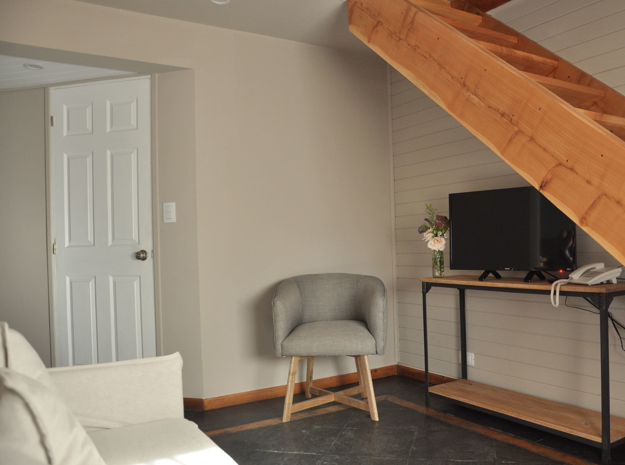 Ein modernes Wohnzimmer mit einem grauen Sessel, einer Holztreppe, einem Fernseher auf einem Holztisch und einer Tür.