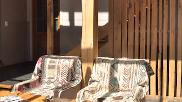 Un espacio de estar al aire libre con asientos de madera, dos sillones acolchados, una mesa de madera con revistas y una valla de madera al fondo.