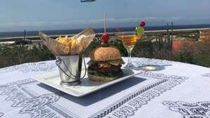 Un plato con una hamburguesa y papas fritas sobre una mesa, con vista al aeropuerto y al océano.
