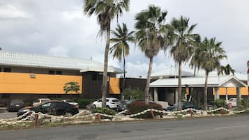Un edificio con fachada amarilla y techo blanco, rodeado de palmeras y automóviles estacionados.