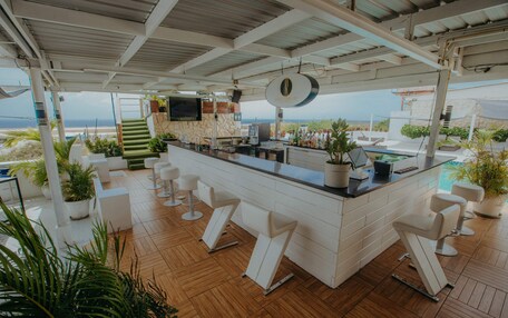 A bar area with a view of the beach, white bar stools, and potted plants.