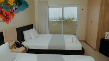 Habitación de hotel con dos camas, un cuadro en la pared, un equipo de aire acondicionado y vistas a través de la puerta de vidrio.