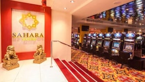 Interior de un casino con una pared roja, un logotipo grande y varias máquinas de juego.
