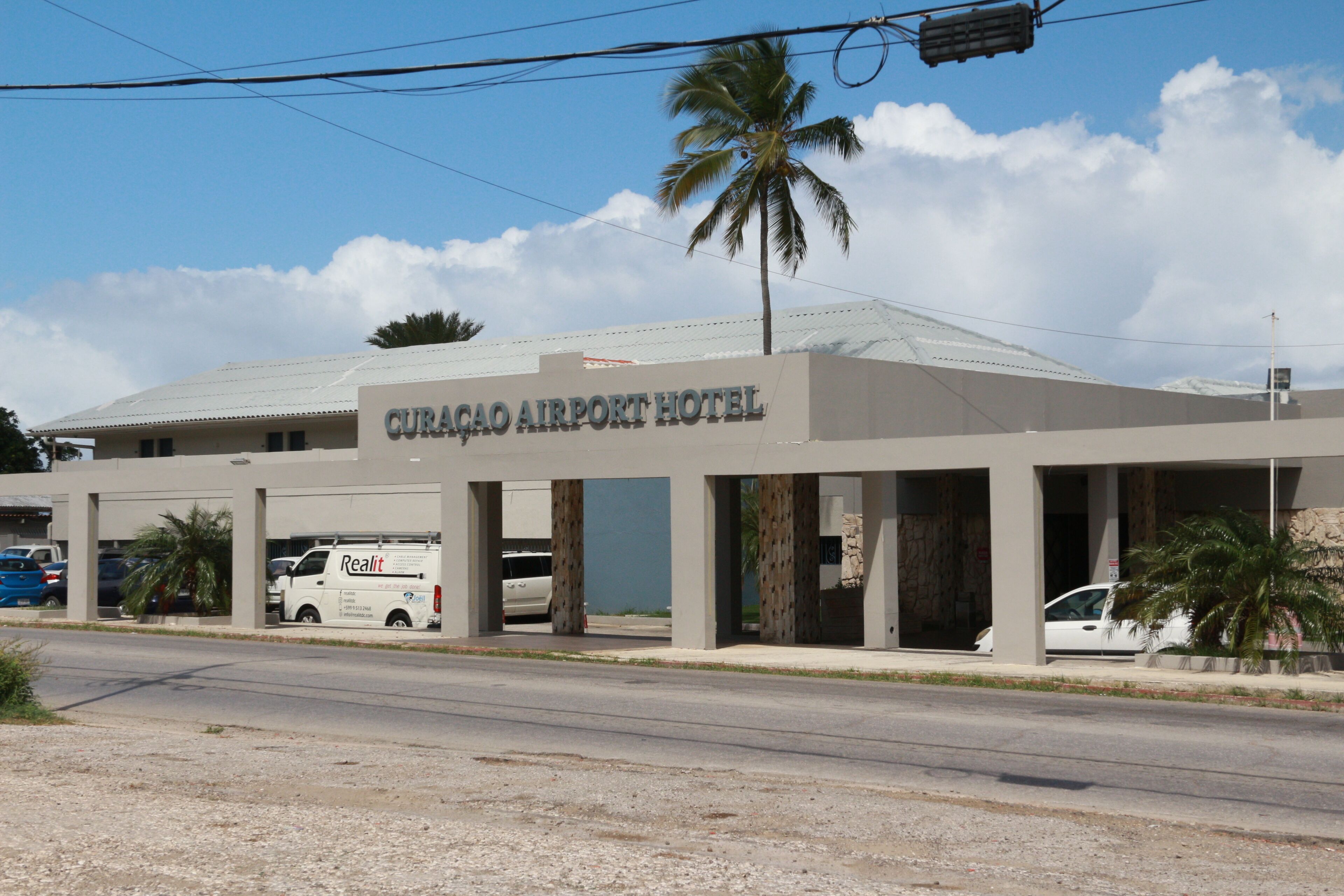 The Curacao Airport Hotel with a van parked in front, palm trees, and a clear sky.