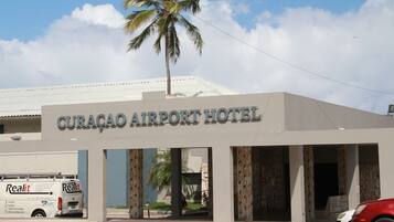 Exterior del Hotel Curacao Airport, con un letrero, una palmera y una furgoneta estacionada frente al hotel.
