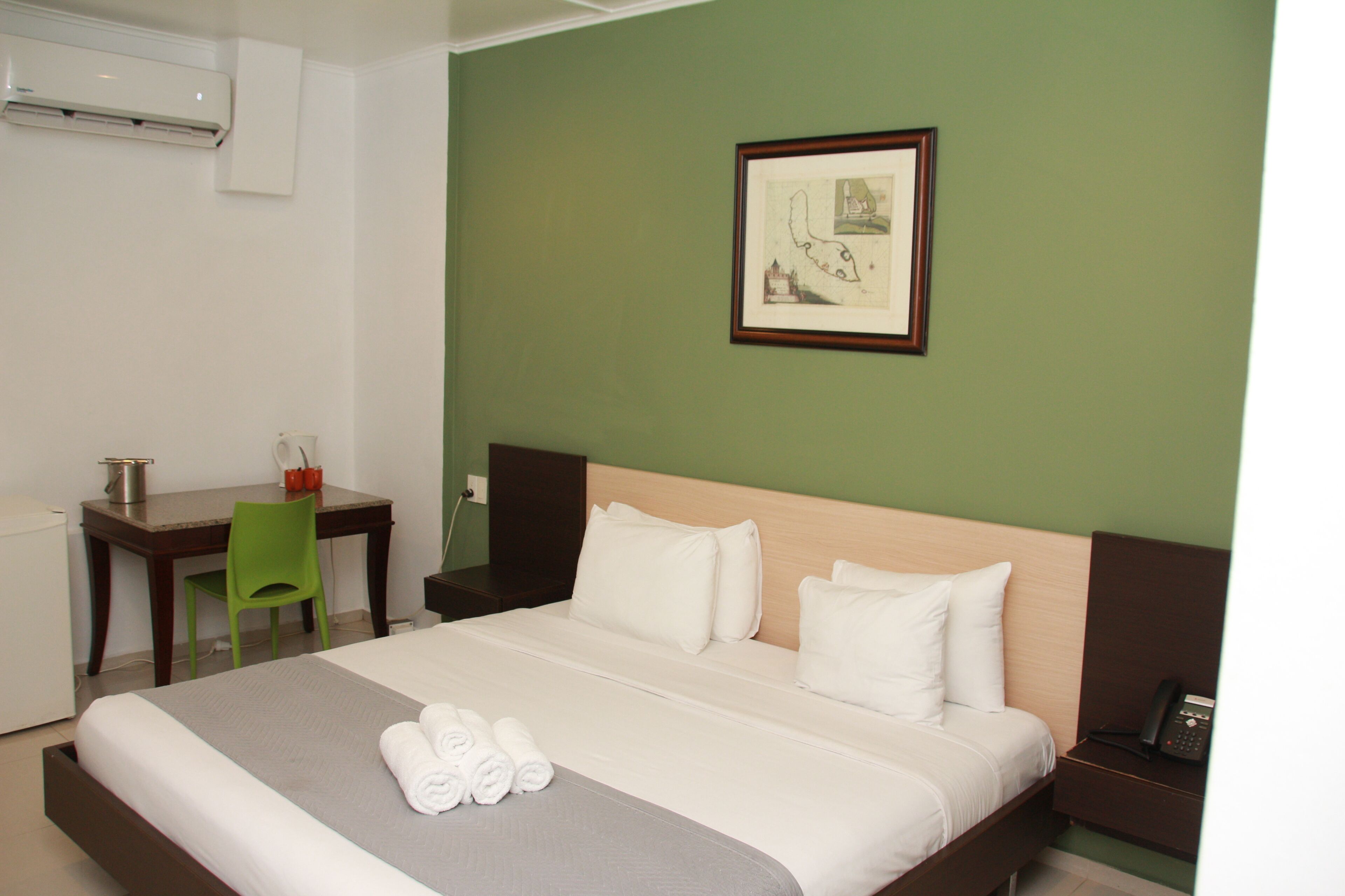 Una habitación de hotel con una cama, un escritorio, una silla, una mesita de noche y un cuadro en la pared.