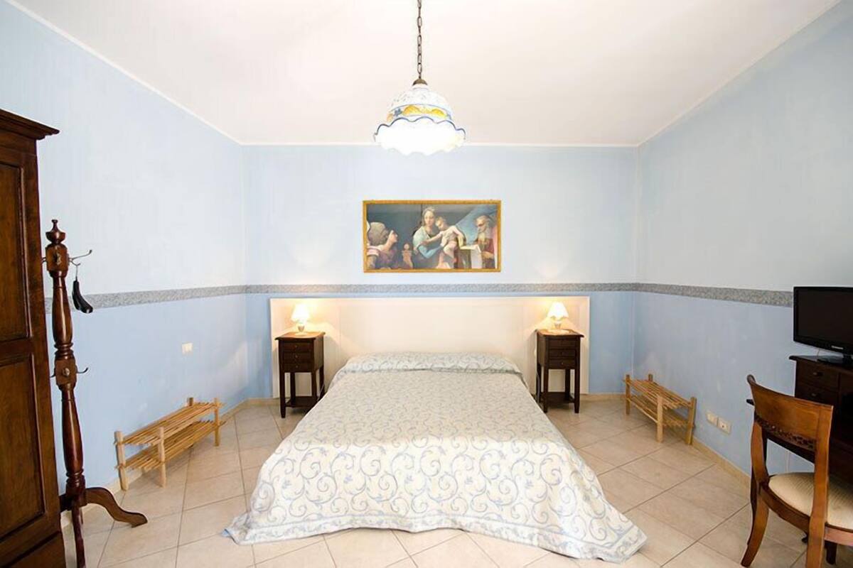 A bedroom with a bed, bedside tables, a chair, a television, and a painting on the wall.