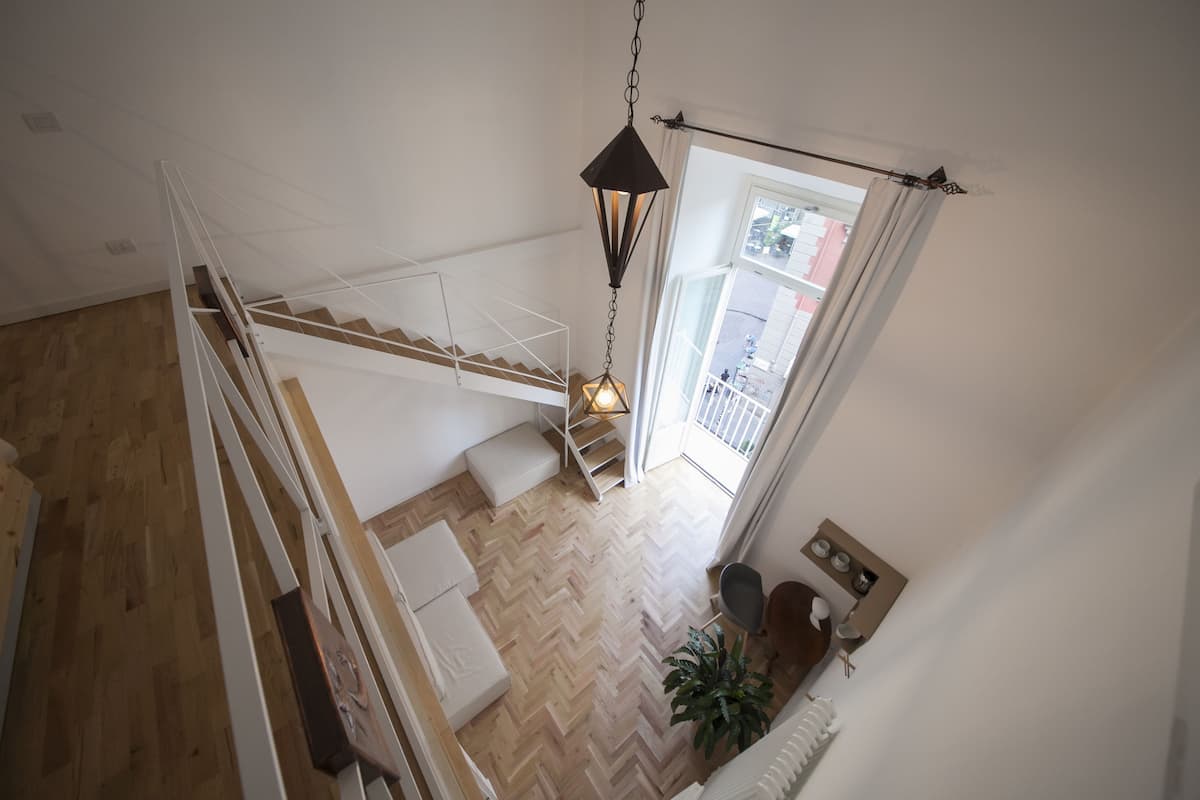 A high-ceilinged room with a wooden herringbone floor, a white staircase, and a hanging light fixture.
