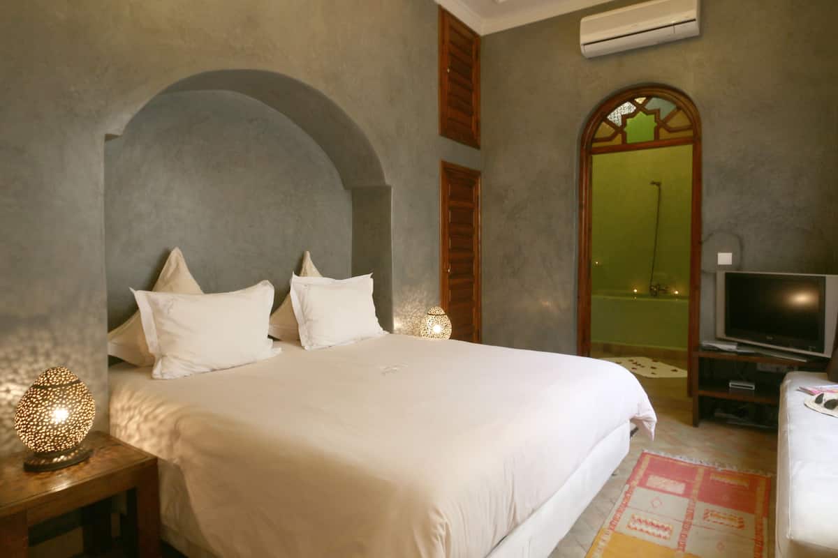 A hotel room with a large bed, a television, and a bathroom visible through an arched doorway.