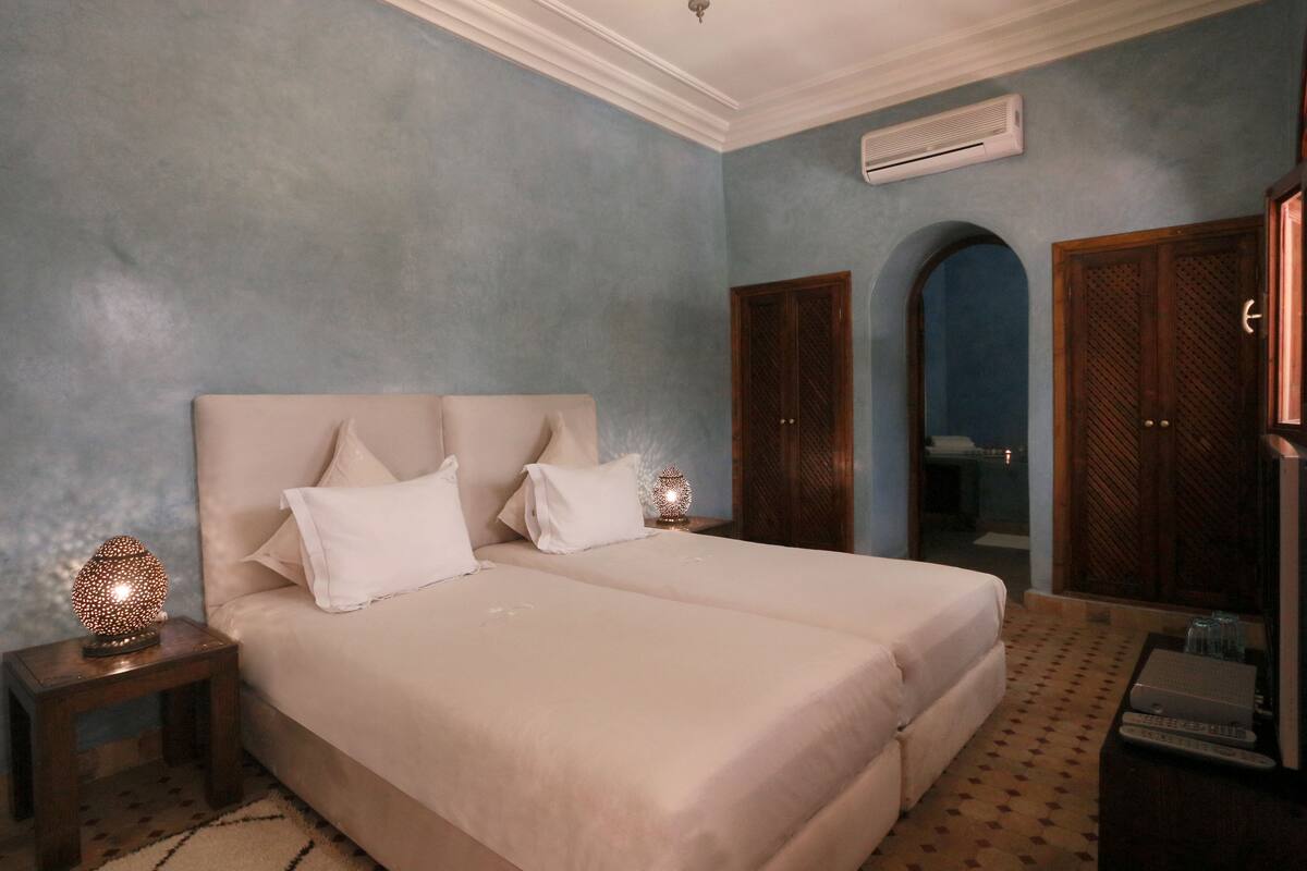 A bedroom with two beds, a nightstand with a lamp, and a wardrobe.