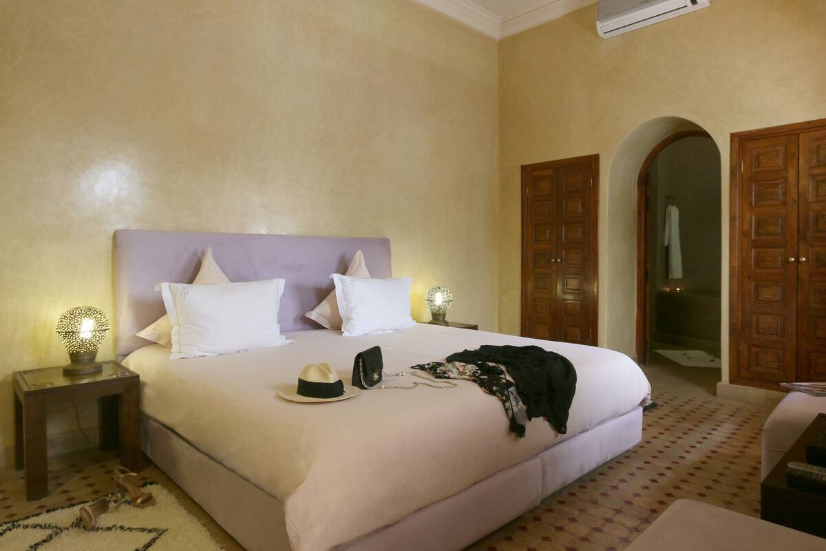 A neatly made bed with white linens, a small bedside table with a lamp, and a door leading to another room.