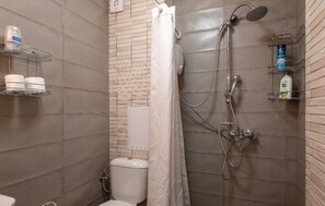 Une salle de bain équipée d’une douche, de toilettes et d’étagères où sont rangés les articles de toilette.
