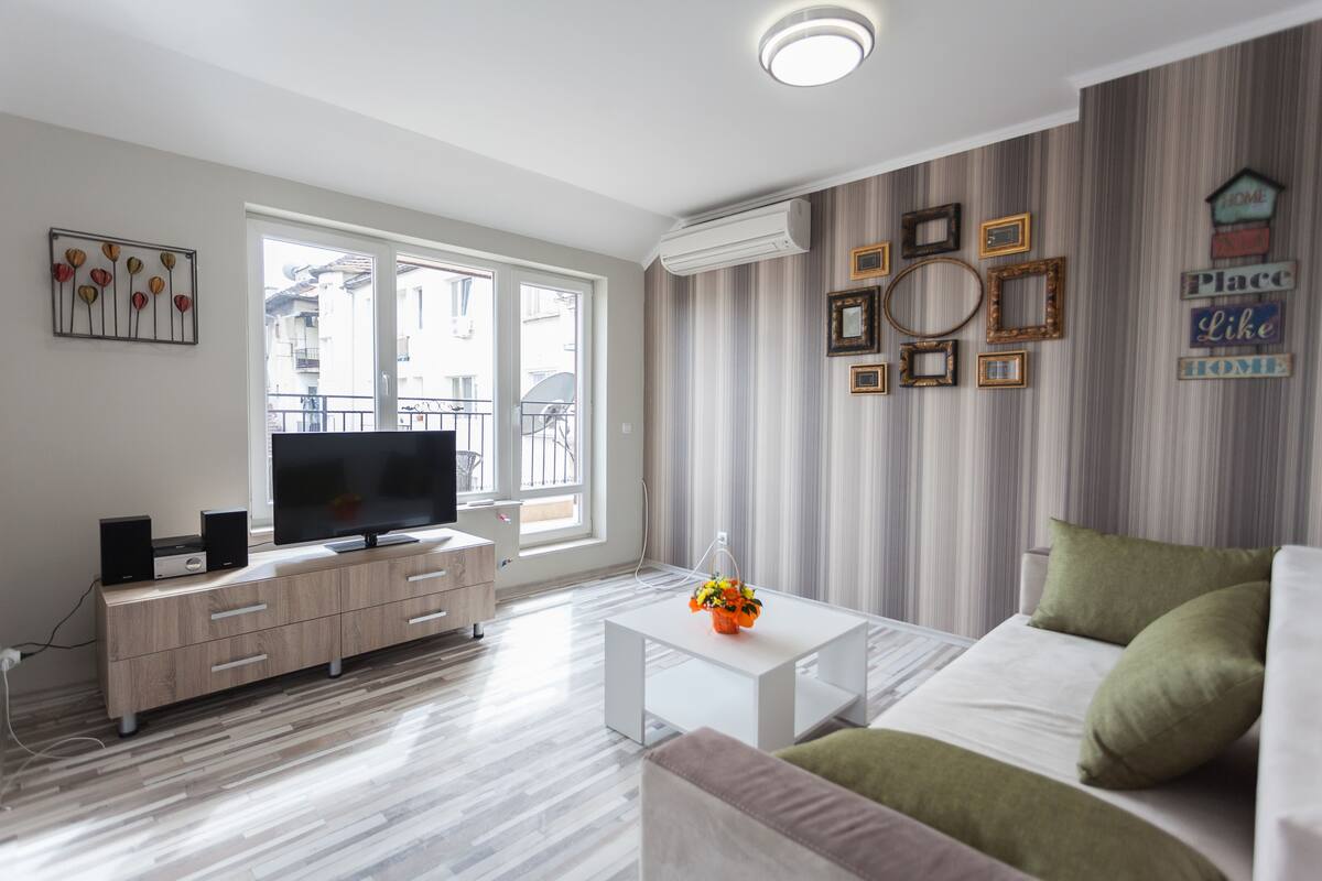 A modern living room with a flat-screen TV, wooden cabinet, white coffee table, and green sofa.
