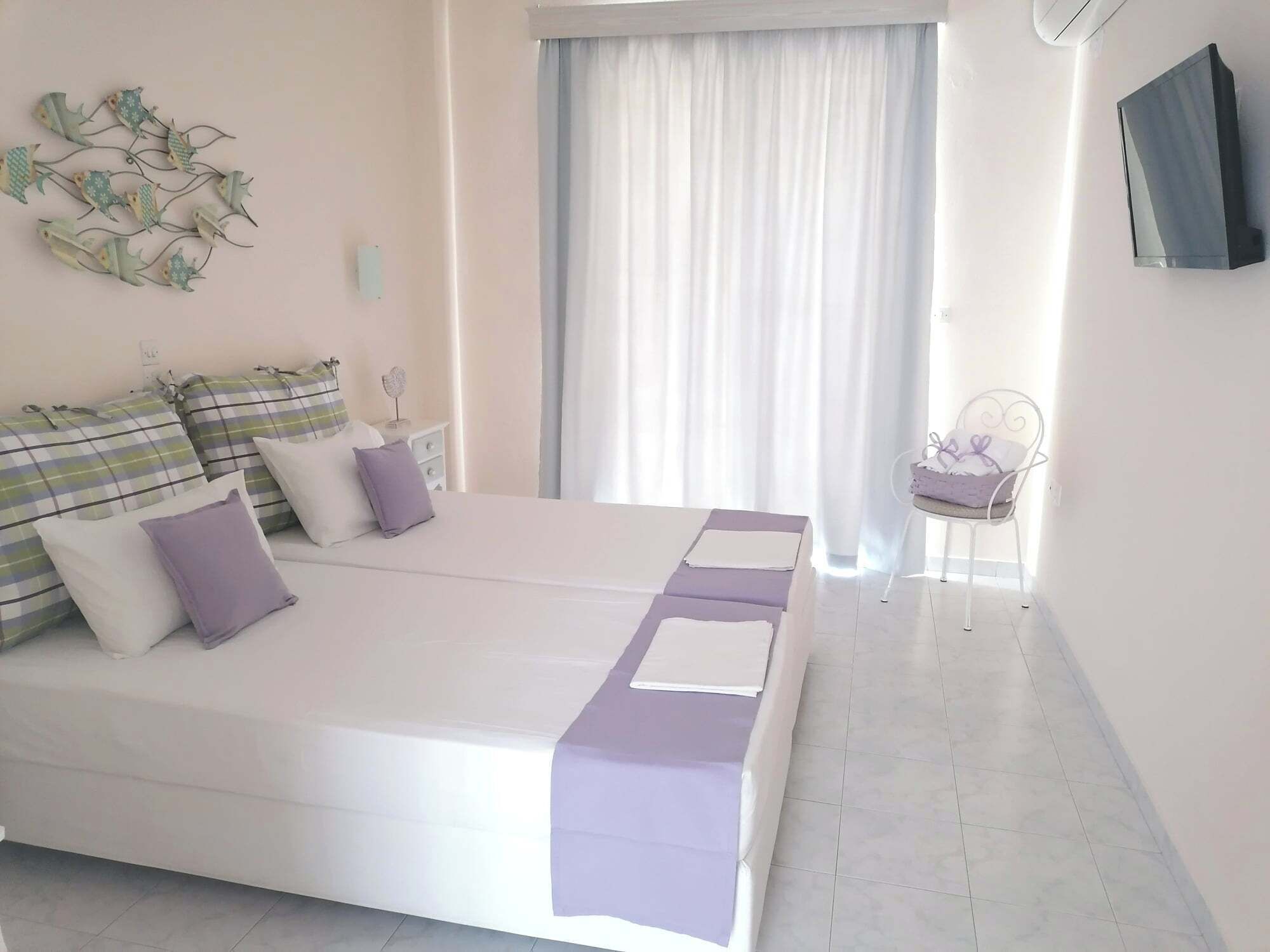 A bedroom with a double bed, a chair, a TV, and a window with curtains.