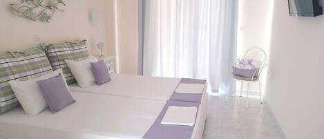 A bedroom with a double bed, a chair, a TV, and a window with curtains.