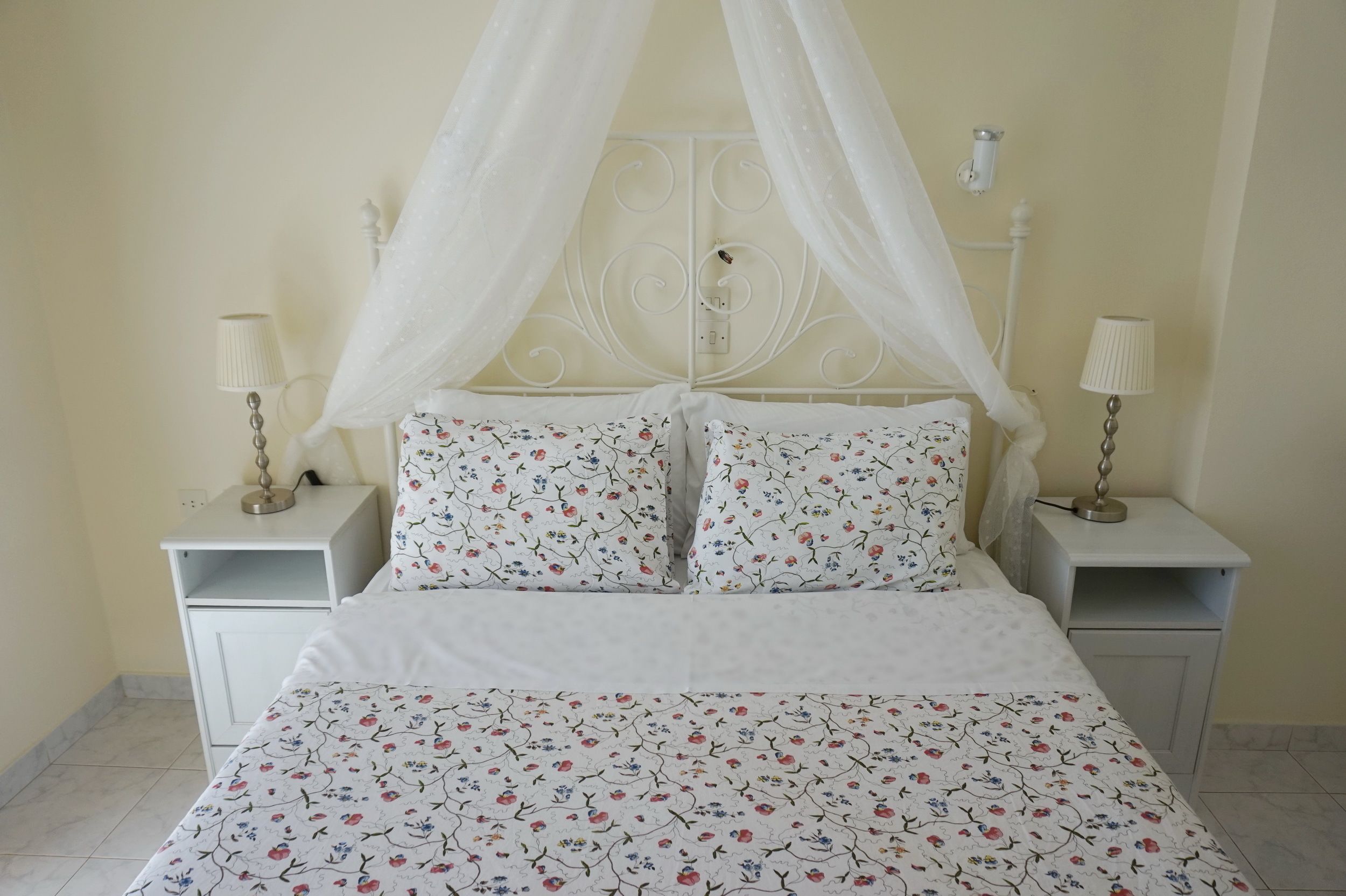 Een bed met hemelbed, beddengoed met bloemenprint en twee nachtkastjes met lampen.